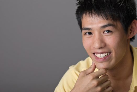 Smiling Asian young man, closeup portrait with copyspace on gray.