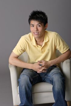 Young man sit on chair, closeup portrait over gray background.