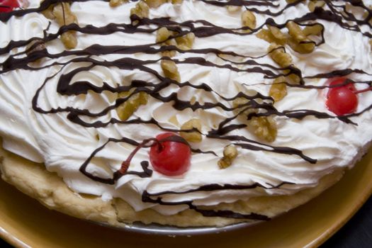 Close up of a bannana cream pie with chocolate drizzled over the top and nuts and cherries