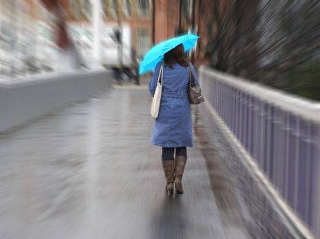 Girl walking in the rain with umbrella, dressed in a blue mac with an azure umbrella