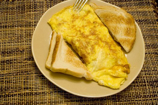 Omelette and white toast on a tan plate on a wicker placemat