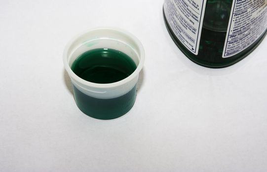 A cup of green Cough Syrup with bottle on white 