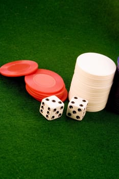 close up of two dice and three stacks of poker chips on green felt