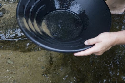 looking for gold in a small stream in northern Michigan by Mackinaw city black pan with sand and gravel in the pan