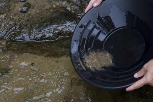 looking for gold in a small stream in northern Michigan by Mackinaw city black pan with sand and gravel in the pan