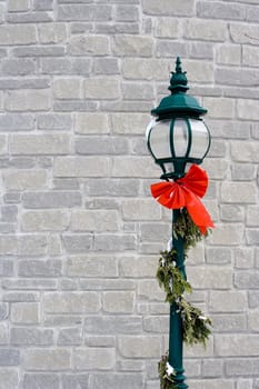green lampost against a white brick wall wrapped in garland with a little snow on it