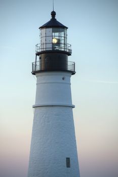 A light house with the light turned on, against a pastel sky