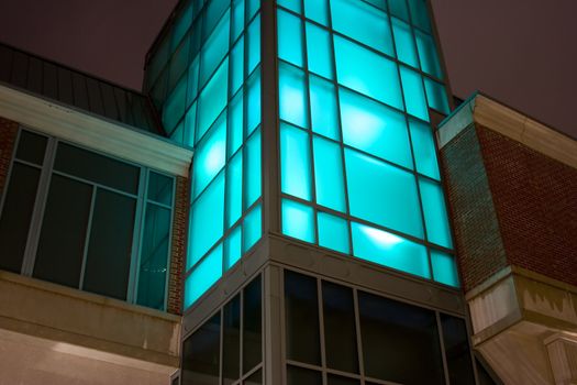 Night shot of glass office building window glass lit with blue purple light room for type above building