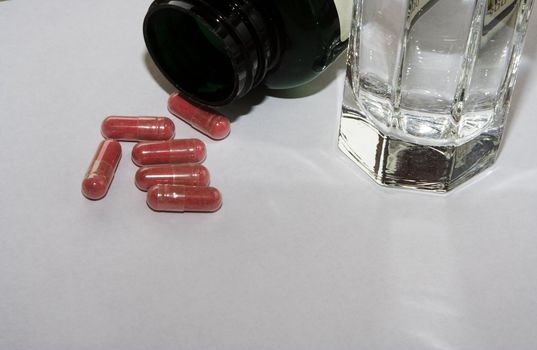 close up of pink pills and bottle with glass of water