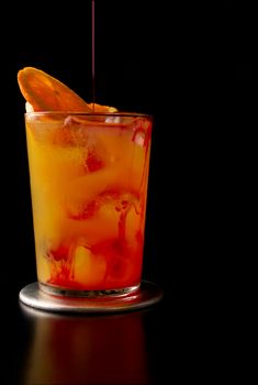 Pouring a tequila sunrise cocktail decorated with an orange slice