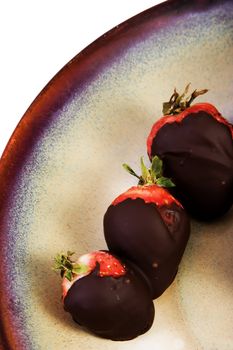 Chocolate covered strawberries on ceramic brown plate on white background