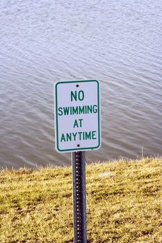 No swimming sign at the edge of a lake overcast day