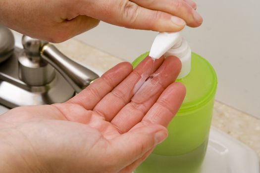 woman washing hand under running water white sink chrome spout putting liquid soap on hands