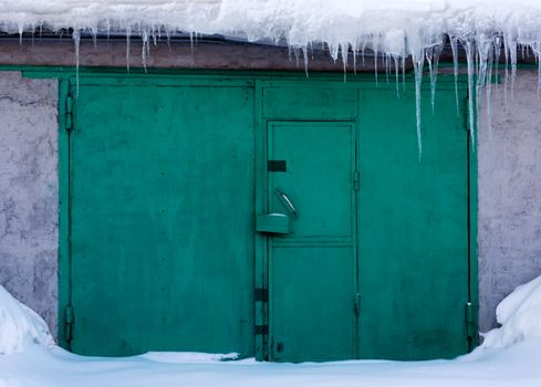 Green gates in snow, icicles droop, lock, doorknob