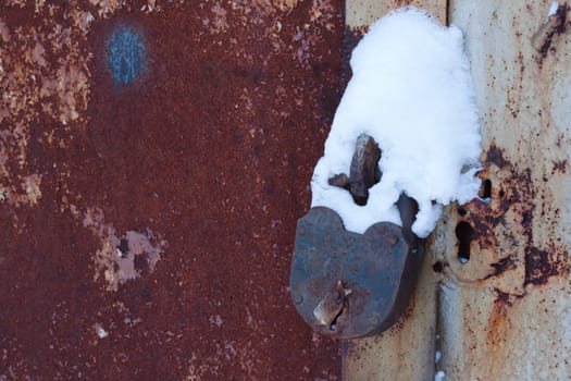 Old, rusty padlock coated by snow, gates