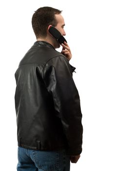 A young man wearing a leather jacket is facing away from the camera and talking on his cellphone, isolated against a white background