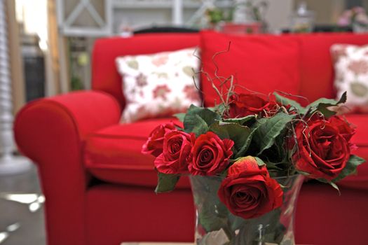 A red sofa in a living room, roses in the foreground 
