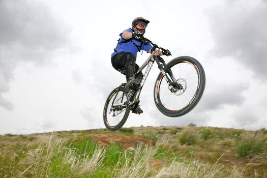 A downhill moutainbiker jumping over a natural ramp

