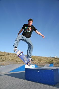 A young skater jumping over a ramp in a park
