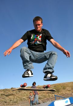 A young skater jumping over a ramp in a park
