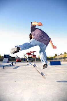 A young skater jumping over a ramp in a park
