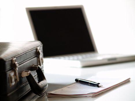 A black leather suitcase, a calender and a laptop
