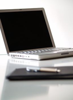 A laptop and a leather folder with a pen on top
