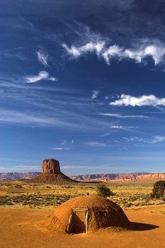 Hogan - the traditional Navajo red clay earth house, with backdrop of famous table mountains of the Navajo National monument on the background