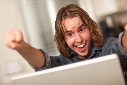 Happy, Cheering Young Man Using A Laptop Computer and Cheering with Fists in the Air.