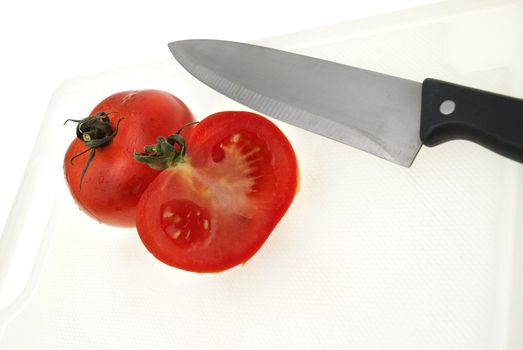 Cutting white plastic board with a knife and tomato isolated on a white background.
