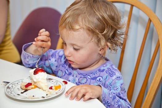 Cute little European toddler girl enjoying a piece of birthday cake.