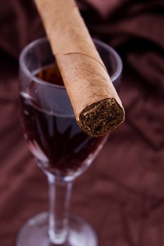 Cigar on the glass with alcohol on brown