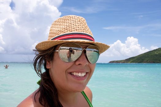 Woman smiles in the tropical Caribbean ocean on the  island of Culebra. Man taking her photo is shown in the reflection of her sunglasses.