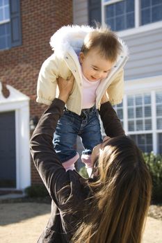 Caucasian mother holding up baby girl in front of house outside.