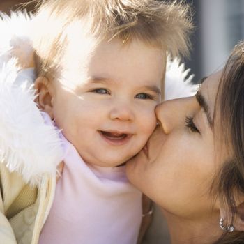 Caucasian mother holding and kissing smiling baby girl.