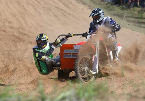 Competitions on cross-country race: 2 persons going on a motorcycle on sand