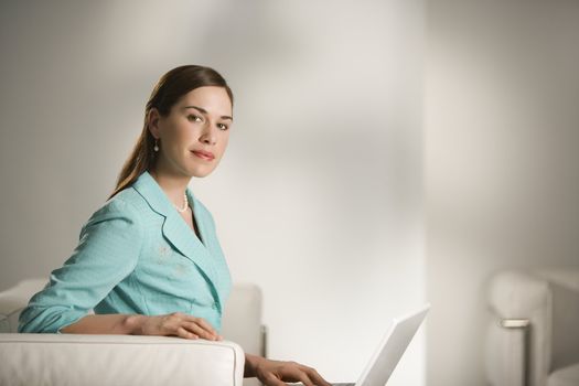 Caucasian mid adult professional business woman sitting in modern office working on laptop computer looking at viewer.