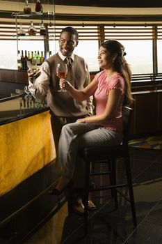 Mid adult African American man and Hispanic woman toasting at bar.