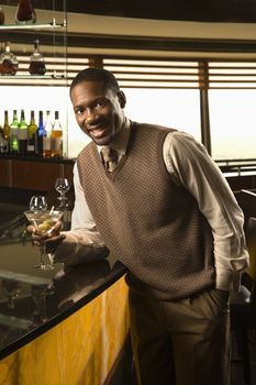 African American mid adult man leaning on bar with martini looking at viewer.