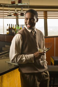 African American mid adult man standing at bar with martini.