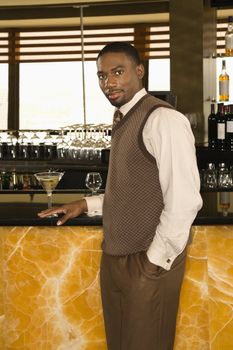 African American mid adult man standing at bar with martini looking at viewer.