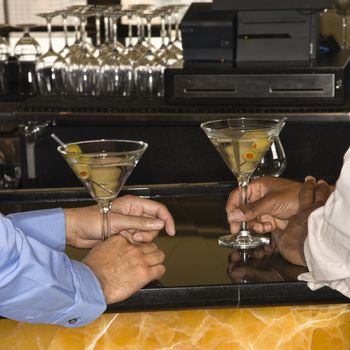 Male hands holding martinis at bar.
