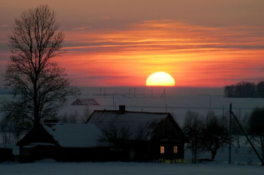 Rural house in the winter evening in beams of the coming sun