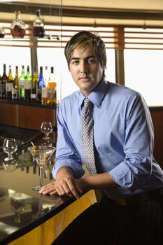 Hispanic mid adult man leaning on bar with martini looking at viewer.