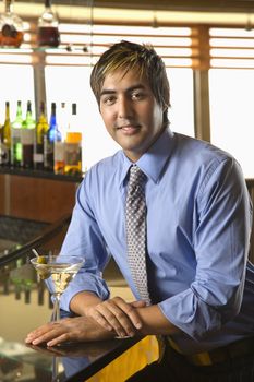 Portrait of Hispanic mid adult man leaning on bar with martini smiling at viewer.