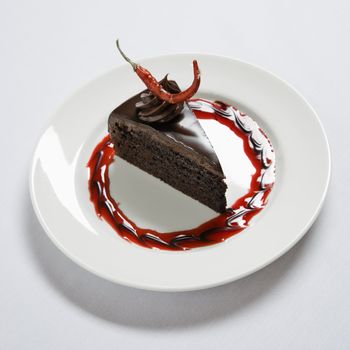 Slice of chocolate cake on dessert plate adorned with a red chili pepper.