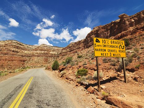 Road sign warning steep grade through rocky Utah landscape.