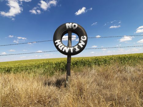 Barbed wire fence with tire reading No Hunting in front of agricultural field.