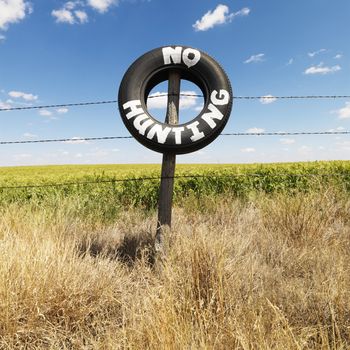 Barbed wire fence with tire reading No Hunting in front of agricultural field.