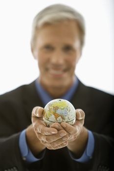 Selective focus of Caucasian middle aged businessman smiling and holding globe towards viewer.